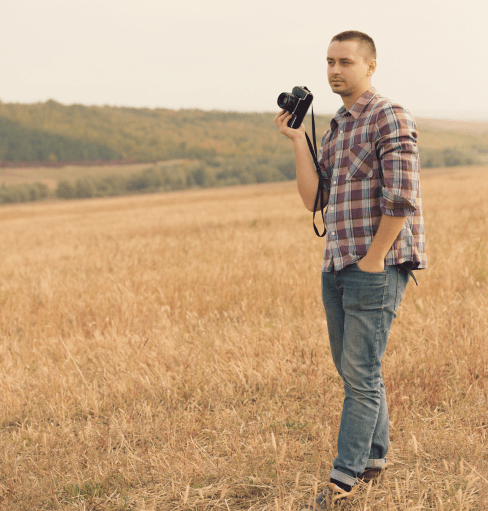 Das Bild zeigt einen auf einem Feld stehenden Mann, der eine Kamera hält und dient als Beispielbild für die Rechte am eigenen Bild/Foto.